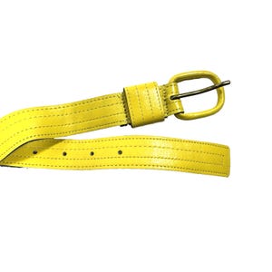 Peut inclure: Une ceinture jaune vif avec une finition lisse et des détails à double couture sur toute la longueur. La ceinture comprend une boucle ovale assortie de couleur jaune avec un ardillon en métal foncé, ainsi qu'une série de trous de réglage.