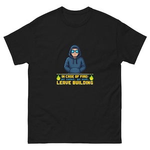 Könnte beinhalten: Ein schwarzes Kurzarm-T-Shirt mit einer Pixel-Art-Grafik einer Person in einem blauen Kapuzenpullover und Sonnenbrille. Unter der Figur steht der Text: IN CASE OF FIRE: git commit, git push, LEAVE BUILDING, flankiert von zwei kleinen grünen Flammensymbolen.