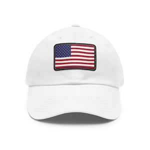 May include: A white baseball cap featuring a rectangular patch on the front panel. The patch displays the United States flag with its characteristic blue canton containing white stars and alternating horizontal red and white stripes with a black border.