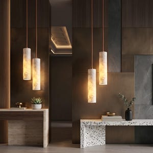 May include: Four cylindrical pendant lights with a white marble pattern and warm internal illumination suspended by thin copper-toned cords. The lights are arranged in pairs, hanging above two separate console tables made of wood and stone.