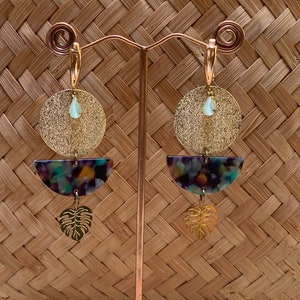 May include: Gold hoop earrings with a textured gold circle, a multi-colored semi-circle, and a gold leaf charm.