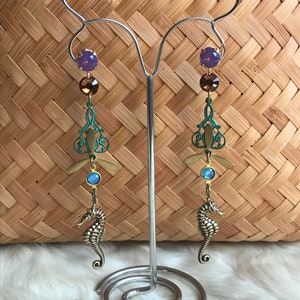 May include: A pair of dangle earrings with a seahorse charm, a dragonfly design, and purple, brown, and blue crystals.