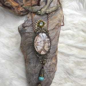 May include: A steampunk-style necklace featuring a brass bird pendant and a large oval pendant with a map design. The necklace includes a green gemstone, turquoise beads, and a faceted aqua crystal. The chain is a copper color.