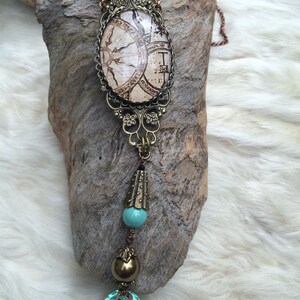 May include: A steampunk-style necklace with a vintage map design in an oval pendant. The necklace features a large, faceted, light blue crystal at the bottom, with brass and turquoise accents. A large, yellow-green gemstone sits at the top.