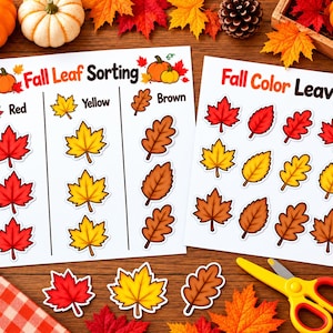 May include: Two white educational activity sheets titled Fall Leaf Sorting and Fall Color Leaves featuring colourful illustrations of red, yellow, and brown autumn leaves, pumpkins, and cut-out leaf shapes with yellow scissors and a glue stick.
