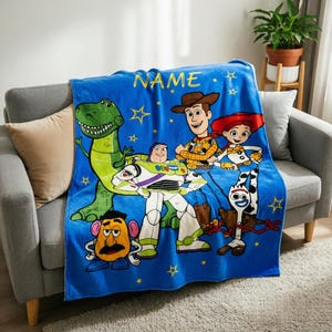 May include: A bright blue fleece blanket featuring a colourful graphic print of Toy Story characters including Rex, Buzz Lightyear, Woody, Jessie, Mr. Potato Head, and Forky. The word NAME is printed in yellow at the top with yellow star accents.