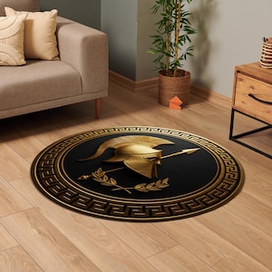 May include: A round area rug featuring a black center with a gold Spartan helmet, a spear, and a laurel wreath. The border displays a gold Greek key pattern. The design is centered on the rug, creating a bold contrast between the black and gold.