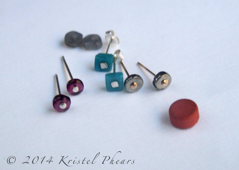 May include: A set of six earrings with various colored glass and metal accents. The earrings are displayed on a white surface.
