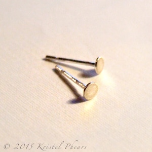 May include: A pair of silver stud earrings with small round discs. The earrings are simple and elegant.