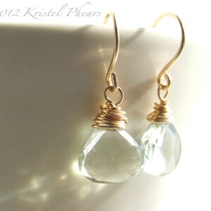 May include: A pair of gold wire wrapped earrings with light green teardrop shaped gemstones.