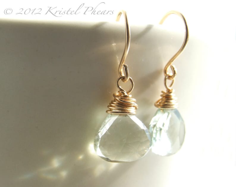May include: A pair of gold wire wrapped earrings with light green teardrop shaped gemstones.
