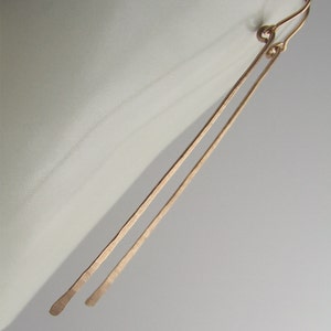 May include: A pair of long, thin, gold earrings with a simple, minimalist design.
