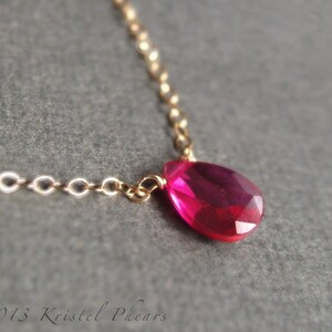 May include: A delicate gold chain necklace with a single teardrop-shaped pink gemstone pendant.
