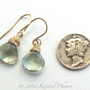May include: A pair of gold wire wrapped earrings with light green teardrop shaped gemstones. The earrings are shown next to a US dime for size comparison.