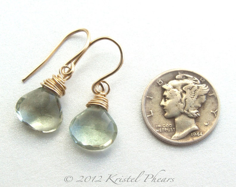 May include: A pair of gold wire wrapped earrings with light green teardrop shaped gemstones. The earrings are shown next to a US dime for size comparison.