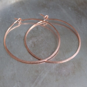 May include: A pair of rose gold hoop earrings. The hoops are thin and delicate, and they are made of a smooth metal.