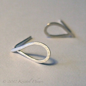 Könnte beinhalten: Ein Paar silberne Ohrringe in Tropfenform. Die Ohrringe sind aus dünnem Metall gefertigt und haben eine gebürstete Oberfläche.