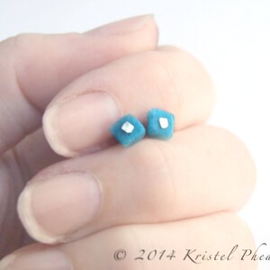 May include: A pair of small, square-shaped earrings with a turquoise blue color and a silver accent in the center.