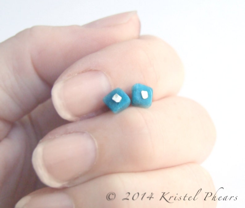 May include: A pair of small, square-shaped earrings with a turquoise blue color and a silver accent in the center.