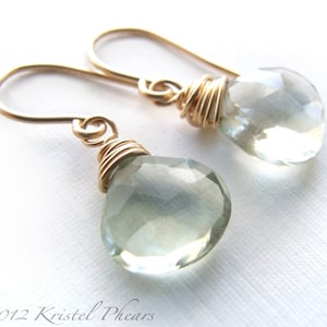 May include: A pair of gold wire wrapped earrings with light green teardrop shaped gemstones.