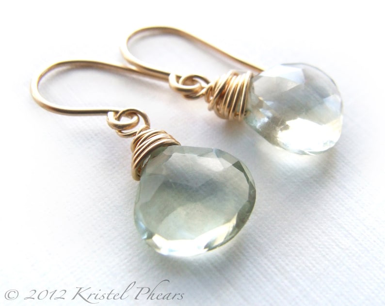 May include: A pair of gold wire wrapped earrings with light green teardrop shaped gemstones.