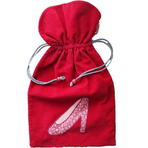 Peut inclure: Un sac en tissu rouge avec cordon de serrage et un motif de chaussure rose brodé.