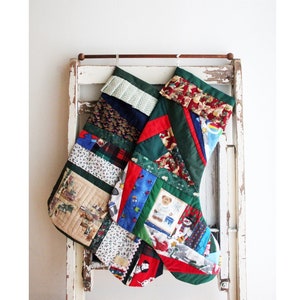 May include: Two patchwork Christmas stockings hanging on a white wooden ladder. The stockings are made of various fabrics in red, green, blue, and yellow. One stocking has a teddy bear design, and the other has a snowman design.