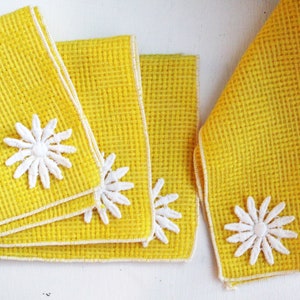 May include: Set of four yellow linen napkins with white embroidered daisy designs. The napkins have a waffle texture and white trim.