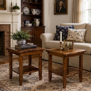 May include: Two square wooden end tables with a dark brown finish, each featuring four straight legs and a lower shelf. The tables are constructed from solid wood with a visible grain pattern and a smooth, polished surface on the tabletop.
