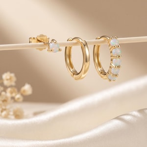 May include: A set of gold-toned jewelry consisting of one stud earring with a single round opal, one plain gold hoop earring, and one gold hoop earring featuring five small round opals set along the outer edge of the circular band.
