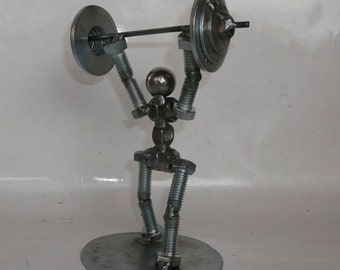 May include: A metal sculpture of a person lifting weights. The sculpture is made of nuts, bolts, and washers. The person is standing on a round metal base.