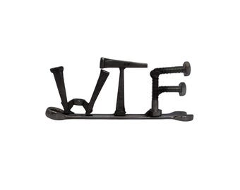 May include: A metal sculpture spelling the letters WTF, constructed from industrial hardware including nails, bolts, and a wrench. The dark gray components are welded together to form the letters, with the wrench serving as a base for the structure.
