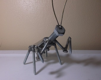May include: A praying mantis sculpture made entirely of metal screws and bolts. The sculpture is silver in color and has a pair of long antennae made of wire.