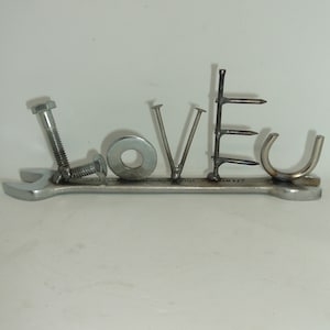 May include: A metal wrench with the word "LOVE" spelled out using various metal hardware, including nails, screws, and a washer.