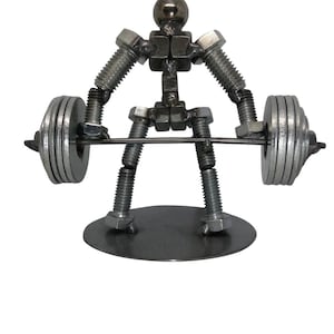 Op de afbeelding: Een metalen sculptuur van een figuur die een halter optilt, geconstrueerd uit diverse stalen hardware-onderdelen zoals bouten, moeren en ringen. Het figuur staat op een ronde metalen voet en houdt een halter met gestapelde ringen.