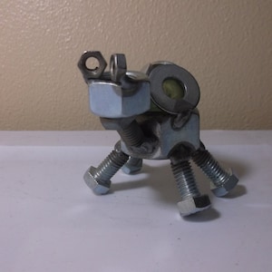 May include: A metal sculpture of an animal, possibly a dog or a frog, constructed from various nuts, bolts, and washers. The sculpture is silver and gray, with a detailed, industrial aesthetic. The legs are made from bolts.