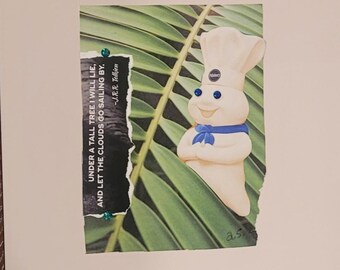 Peut inclure: Un collage représentant le personnage Pillsbury Doughboy avec des yeux en strass bleus, placé sur un fond de feuille de palmier verte. Une bande de papier noire affiche le texte : UNDER A TALL TREE I WILL LIE, AND LET THE CLOUDS GO SAILING BY. -J.R.R. Tolkien.