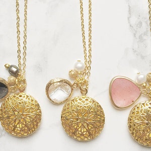 May include: Three gold necklaces with intricate filigree pendants and various charms. Each pendant features a different colored stone: gray, clear, and pink.