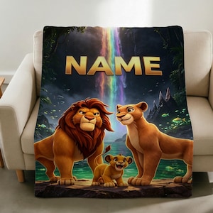 May include: A rectangular fleece blanket featuring a colourful illustration of two adult lions and a lion cub standing on a rock near water. A vibrant rainbow waterfall flows in the background. The word NAME is printed in large gold letters at the top.