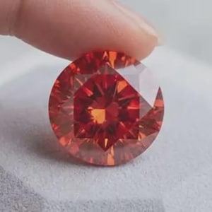 Könnte beinhalten: Ein runder, facettierter Edelstein in einer tiefen, leuchtend roten Farbe. Der Stein weist einen komplexen, symmetrischen Schliff auf, der ein sternförmiges Muster aus Lichtreflexionen auf der Oberfläche erzeugt und brillant, transparent wirkt.
