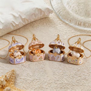 May include: Four gold-tone metal pendants shaped like miniature open trunks, each containing a small animal figurine. The trunks feature colorful enamel designs including a rabbit, a fox, a cat with a star, and a sheep, all on delicate chains.