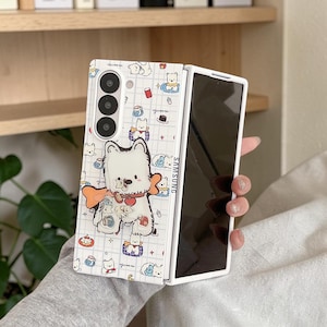 May include: A white foldable smartphone case featuring a grid pattern with small illustrations of white dogs, cups, and cakes. A larger, central graphic depicts a white dog with a red collar and a large orange bone shape behind it. The word SAMSUNG is visible.