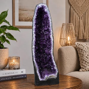 Könnte beinhalten: Eine hohe, vertikale Amethyst-Geode mit tiefvioletten, kristallinen Strukturen in einer dunklen, natürlichen Steinhülle. Die Geode hat einen gezackten, unregelmäßigen Rand und ein hohles Zentrum, das mit funkelnden, facettierten violetten Kristallen gefüllt ist.