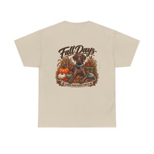 Op de afbeelding: Een beige t-shirt met een afbeelding op de achterkant van een bruine Duitse staande hond, omringd door pompoenen, tarwe en herfstbladeren. De tekst Fall Days staat boven de hond en German Shorthaired Pointer staat onder de illustratie.