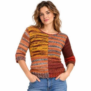 Könnte beinhalten: Ein Strickpullover mit Color-Block-Design und horizontalen Streifen in Senfgelb, gebranntem Orange, Dunkelrot und Grau. Das Kleidungsstück hat Dreiviertelärmel und einen Rundhalsausschnitt und wird mit einer blauen Jeanshose kombiniert.