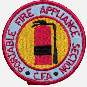 Peut inclure: Un écusson brodé circulaire présentant un graphique d'extincteur rouge sur fond jaune. La bordure bleu clair contient le texte rouge "PORTABLE FIRE APPLIANCE SECTION" et "C.F.A" en bas, le tout entouré d'un bord cousu rouge épais.