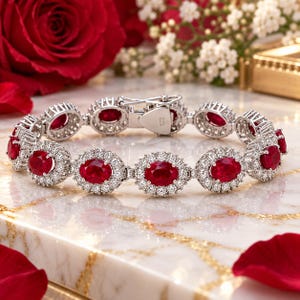 May include: A silver-toned bracelet featuring a series of oval-cut red gemstones, each surrounded by a halo of small, clear, round-cut stones. The bracelet includes a secure metal clasp mechanism and is arranged in a circular display.