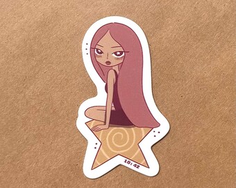 May include: A die-cut sticker featuring a stylized illustration of a character with long pink hair and large eyes, wearing a dark dress. The character is sitting on a tan star with a spiral pattern. The text 10:42 is printed on the star's lower point.