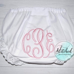 May include: White diaper cover featuring an elastic waistband and leg openings with white eyelet lace trim. The center of the garment displays a large, pink embroidered monogram with the letters C, S, and E. A circular logo reads Stitched by Stephanie.