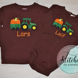 May include: Two brown long-sleeved shirts with a tractor and pumpkin design. One shirt says "Lars" and the other says "Leif" in orange lettering. The tractor is green with yellow wheels, and the pumpkin is orange.